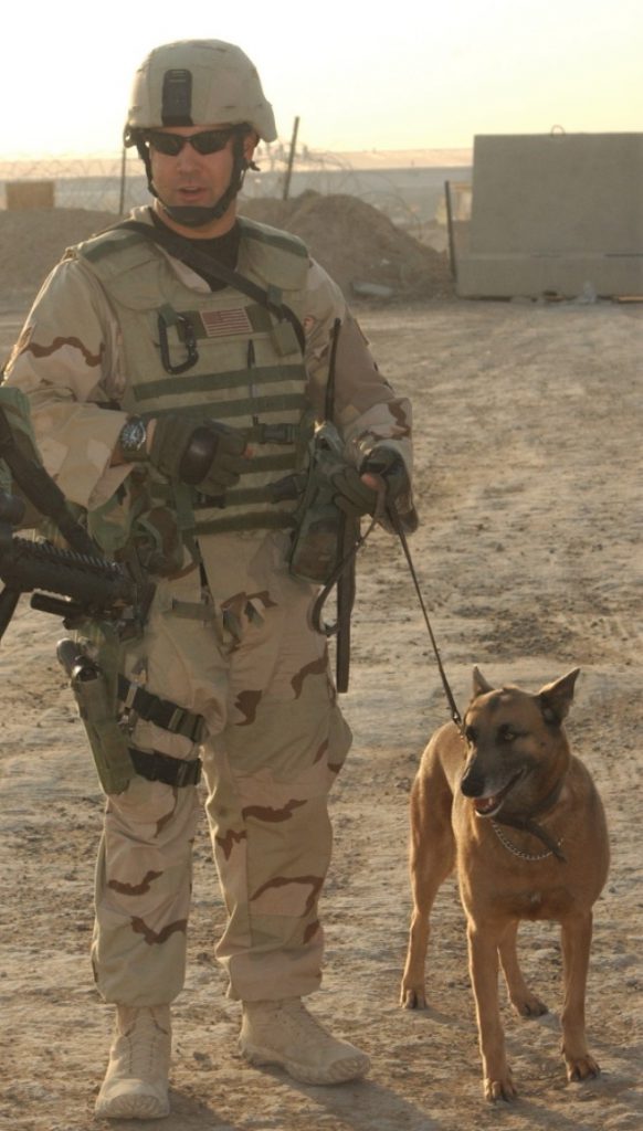 Photo of James Ramondetta in desert camouflage uniform with a German Shepard K-9.