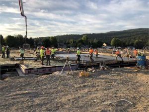 Construction photo of a concrete slab pour. Blue skies, trees and hills in the background. Slightly different angle.