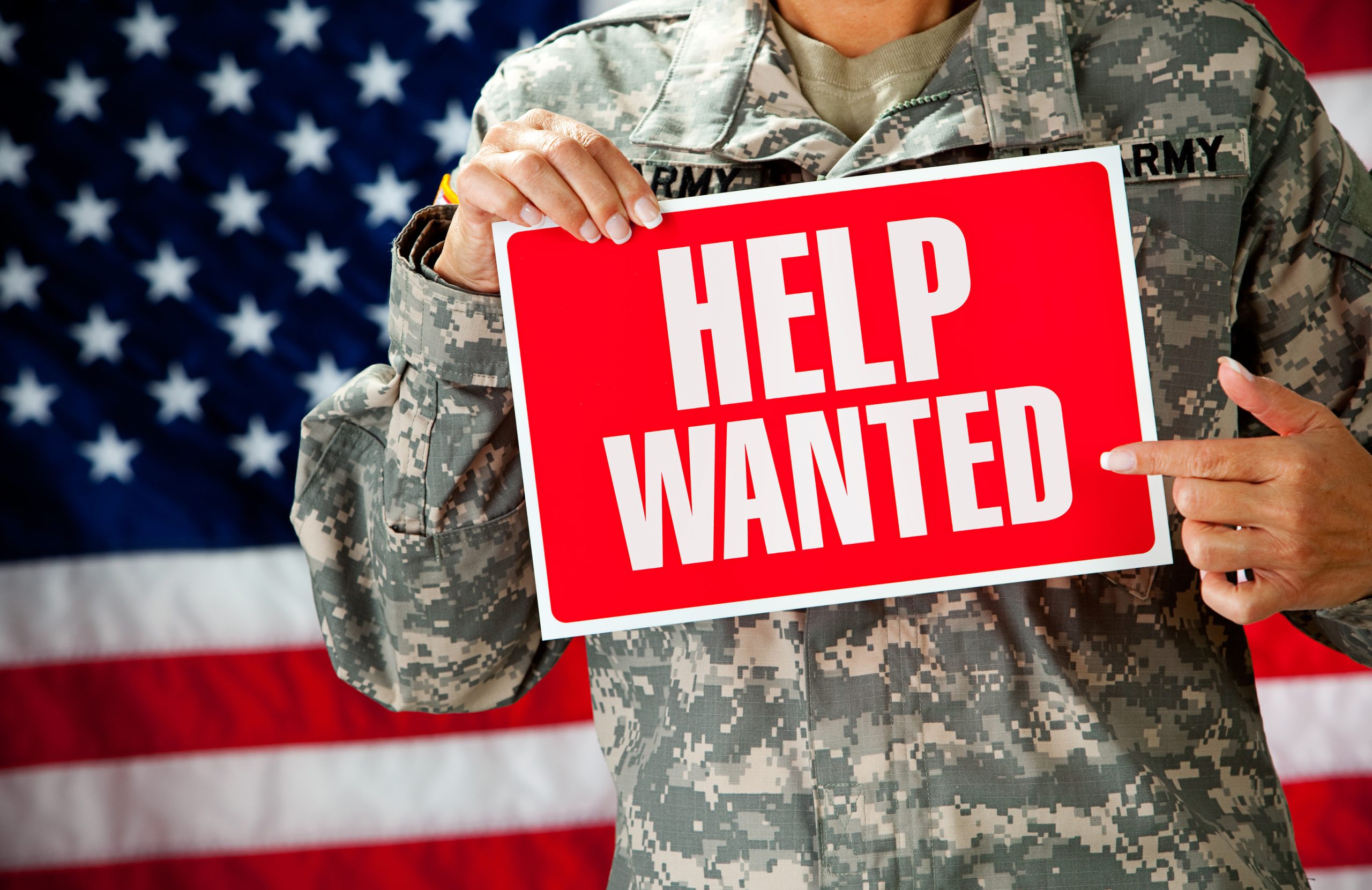 A female soldier in an United States Army uniform.  Holding a help wanted sign.